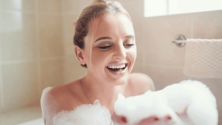 A young woman enjoying a bubble bath for stress relief smiling and happily looking at the foamy bubbles.