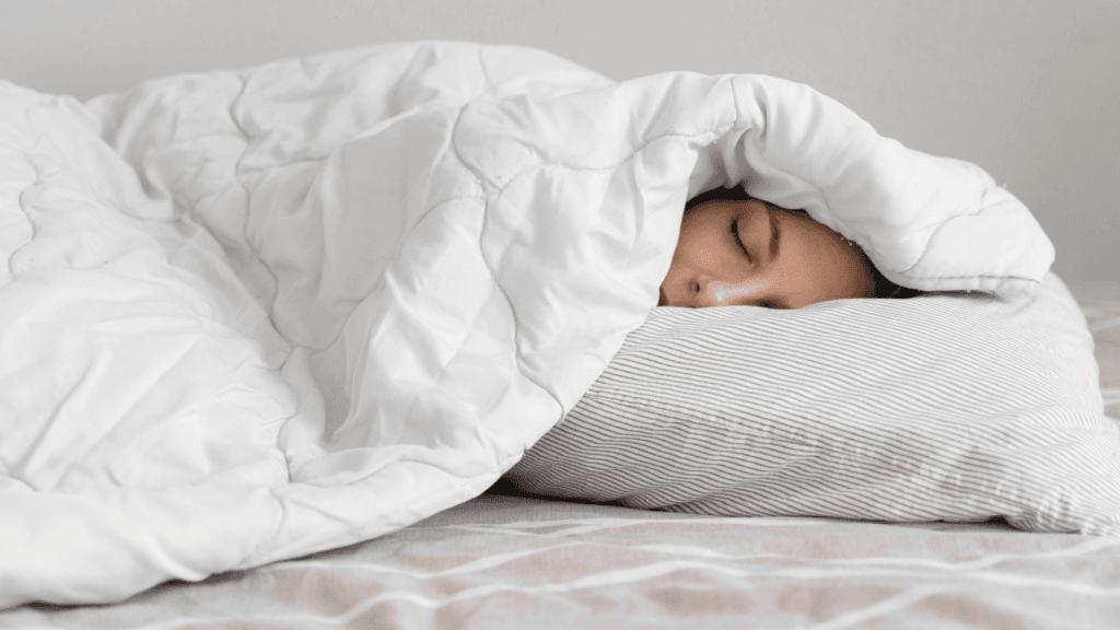 A young woman sleeping peacefully, wrapped in a white weighted blanket, enjoying deep rest.