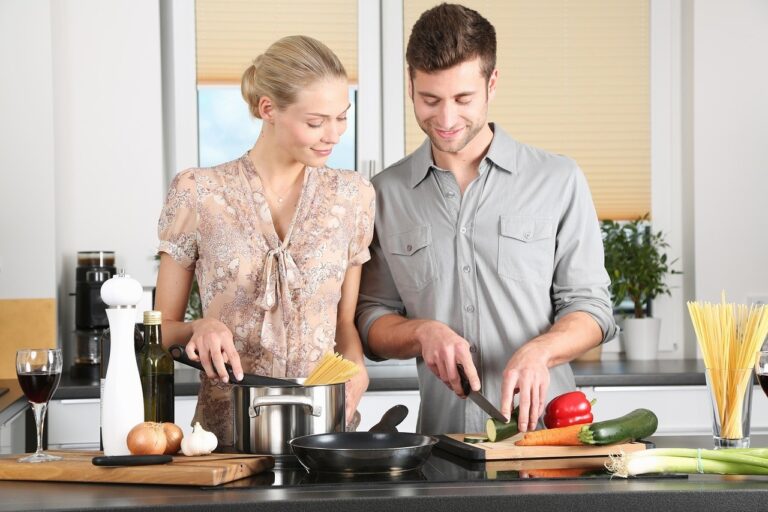 A happy young couple preparing a meal together in the kitchen, with the husband chopping vegetables and the wife watching attentively.